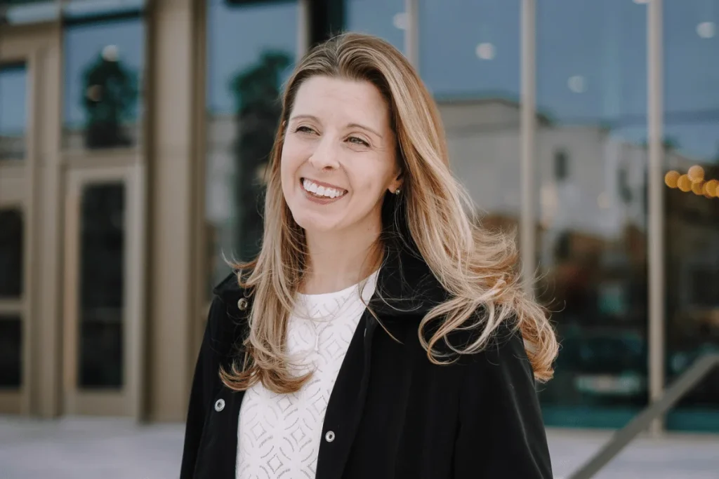 Nora with a bright smile wearing a black jacket outdoors.