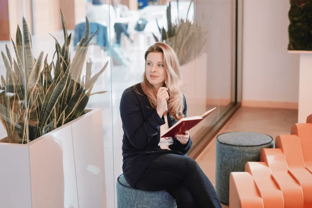 Nora in navy attire pensively seated in a modern office lobby.