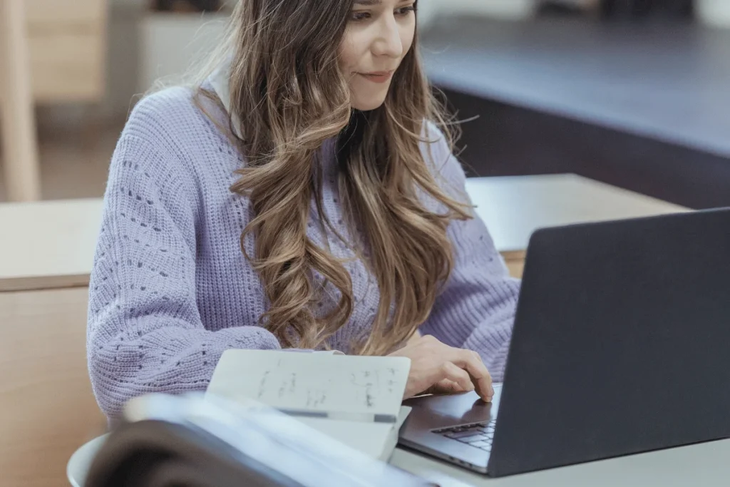 A person in a purple sweater is working on their laptop.