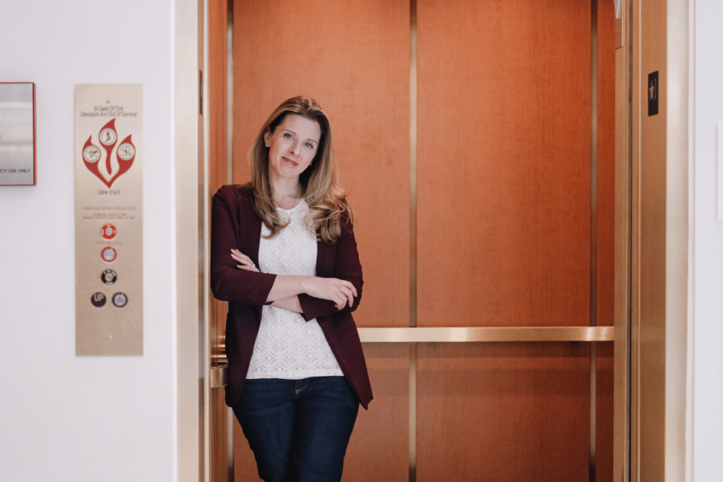 Smiling businesswoman with arms crossed in front of an elevator.