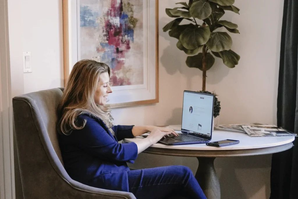 Nora Sudduth works on her laptop in a room with a large abstract painting.