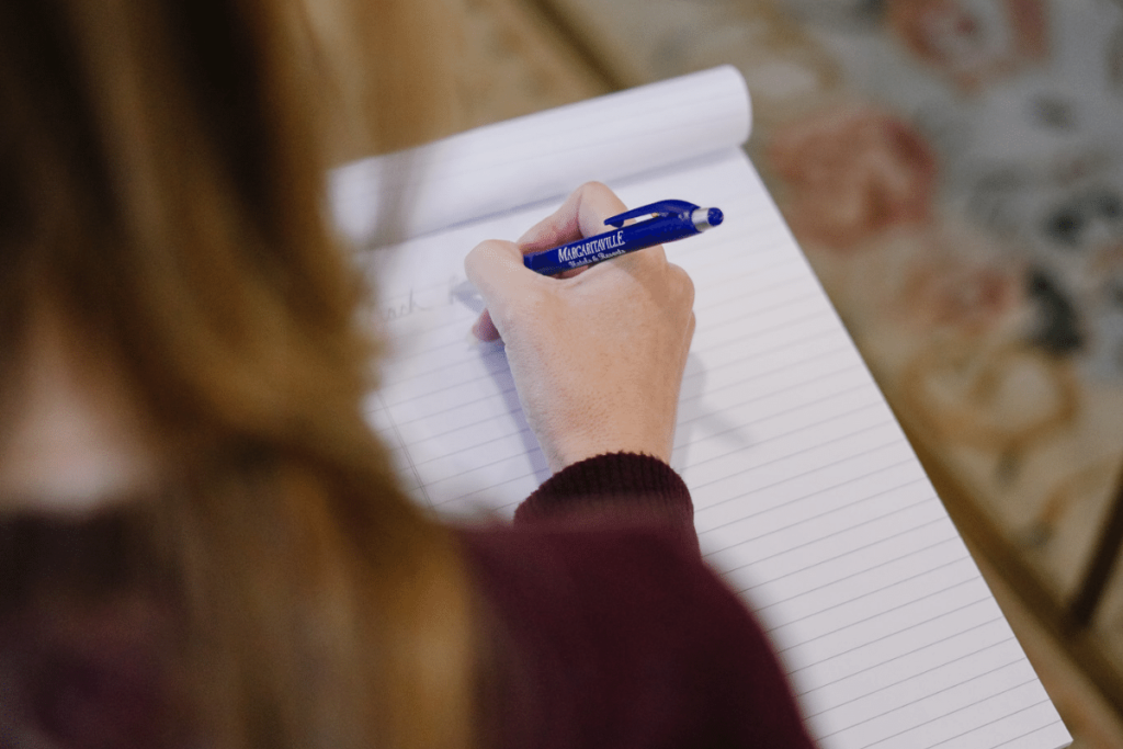 Nora Sudduth writing notes with a blue pen on a lined notepad.