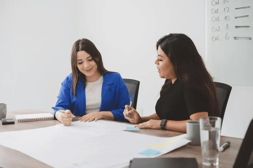 Two women collaborating on project at office table.