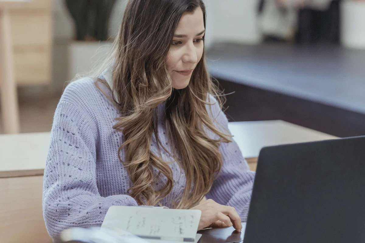 Focused shot of a female professional typing on a laptop, notebook in view.