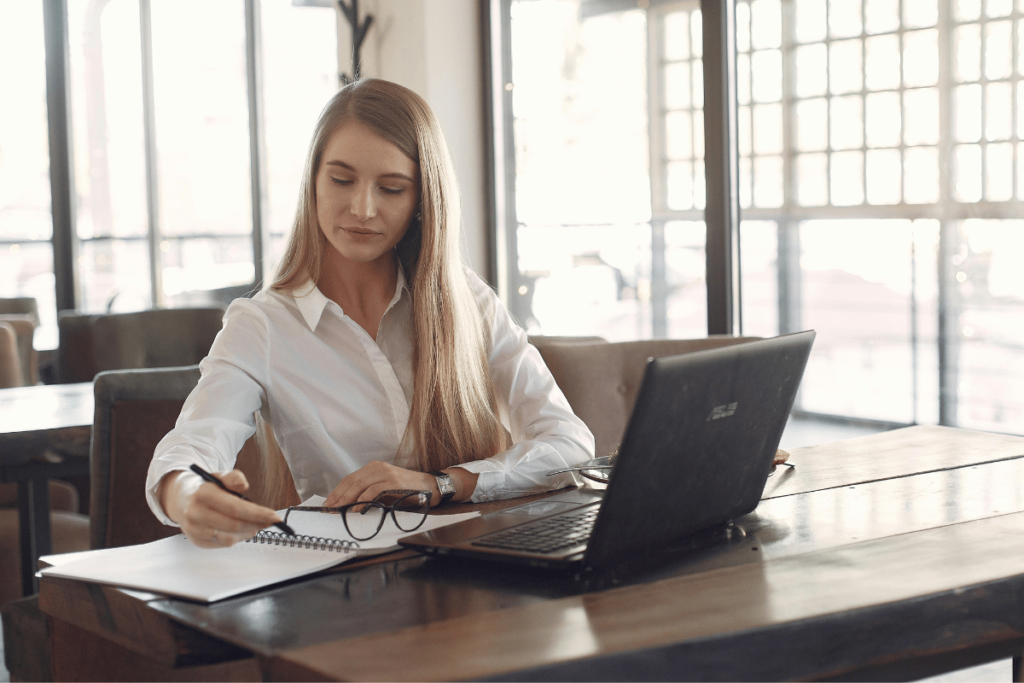 Professional woman taking notes beside a laptop in a bright office.