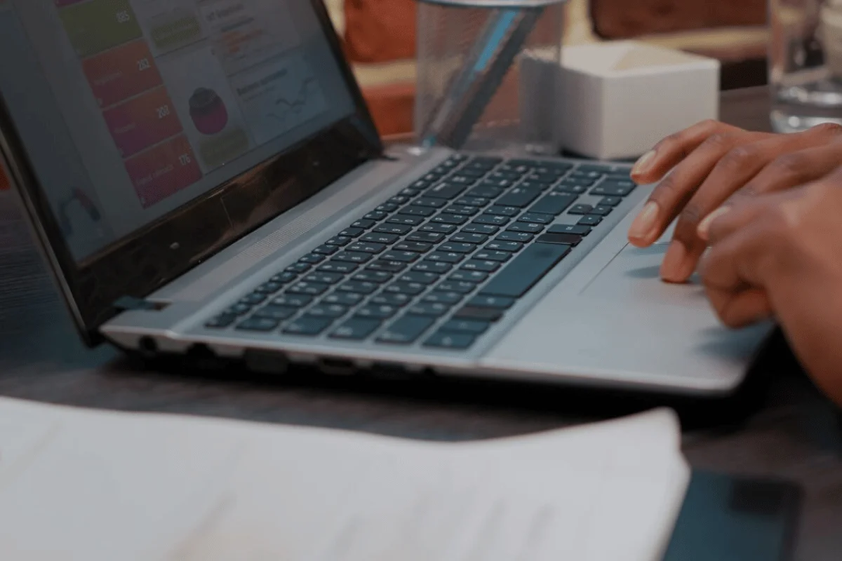 A person using a laptop to work on a desk with a glass of water nearby.