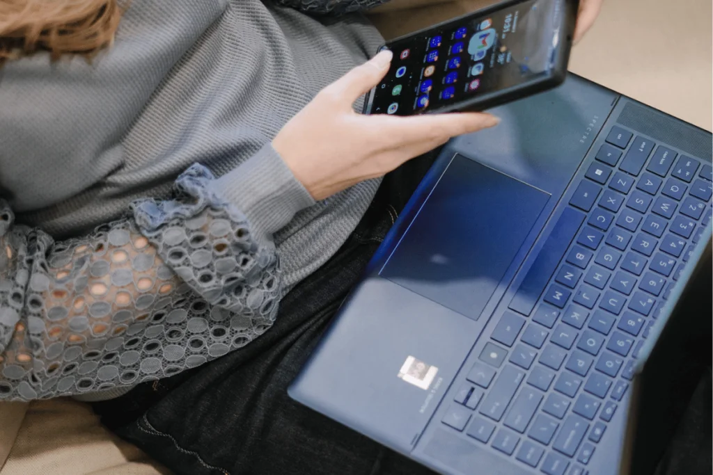 A woman holding a laptop and a cell phone, multitasking with technology.