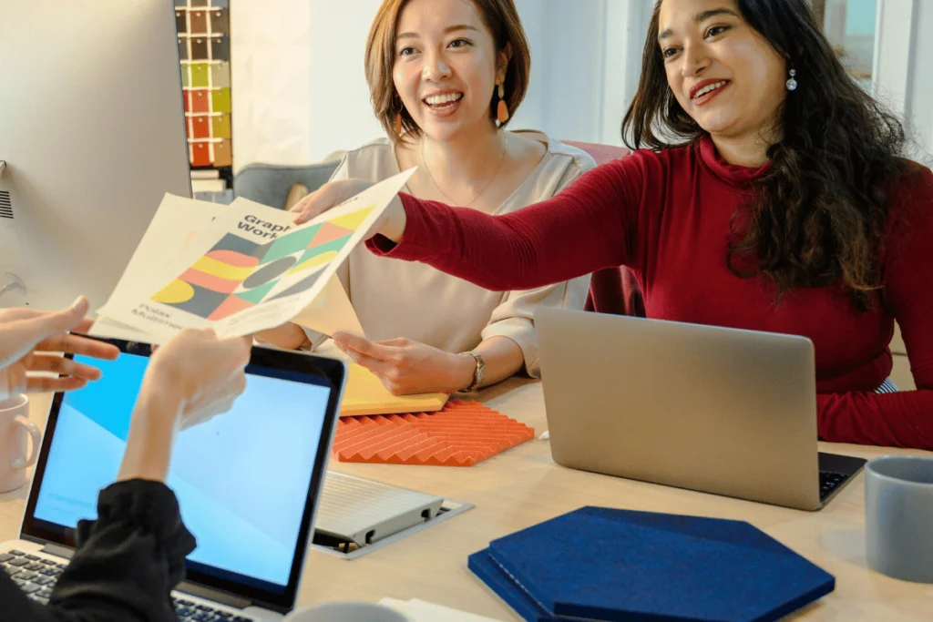 Two smiling women collaborating over a color swatch in a creative office setting.