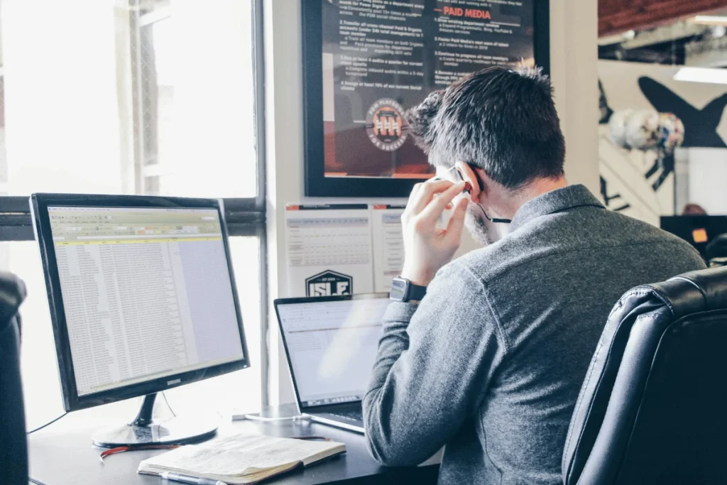 Man wearing a headset, managing data on multiple screens in an office.