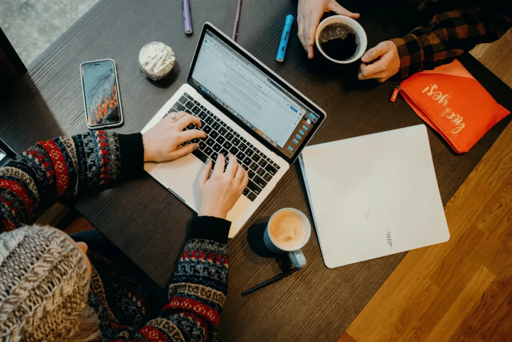 Person typing on laptop with coffee and notebook on desk.