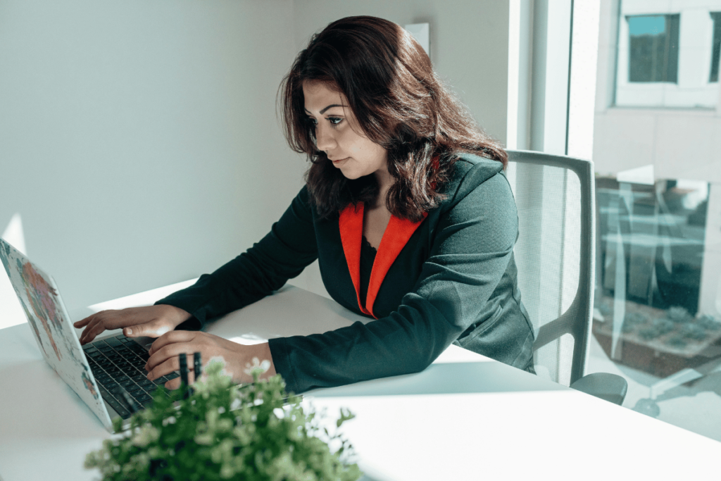 Professional woman in a green blazer typing on a laptop at a white desk.