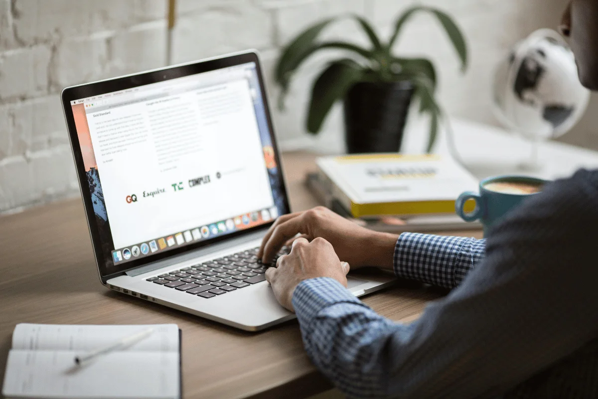 An individual typing on a laptop at a wooden desk in a simple and neat office.