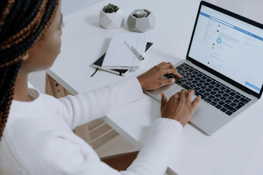 Woman typing on a laptop while checking messages on a professional communication platform.