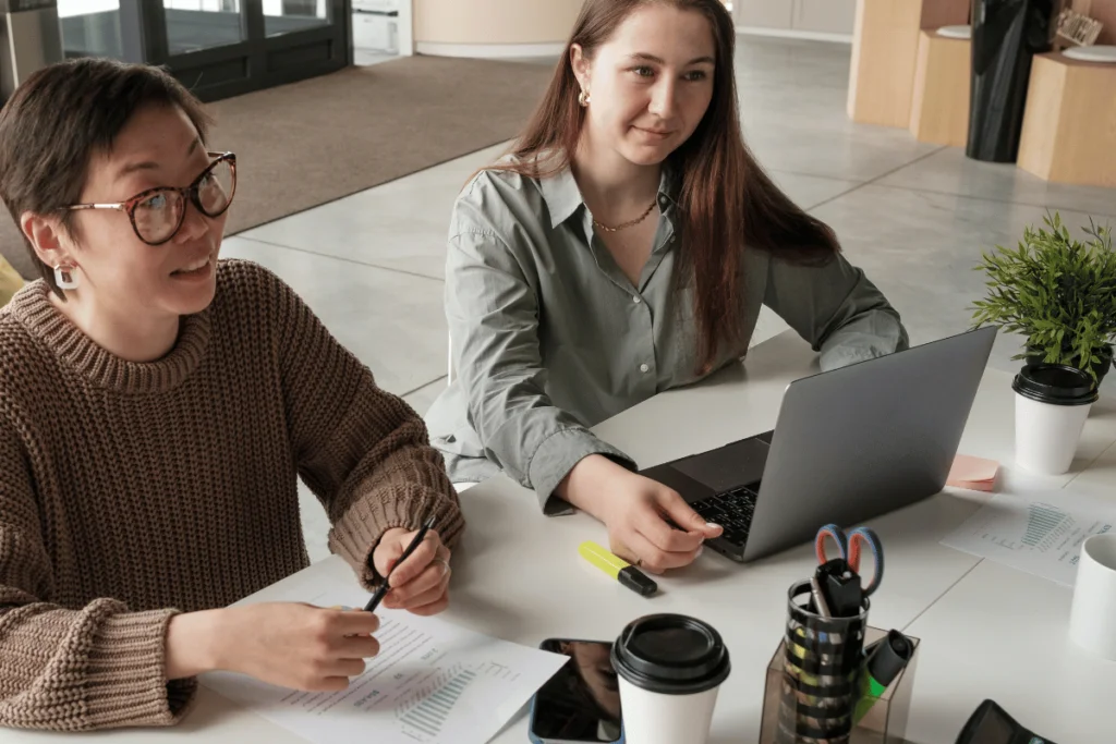 Casual business discussion between two female coworkers at a desk.