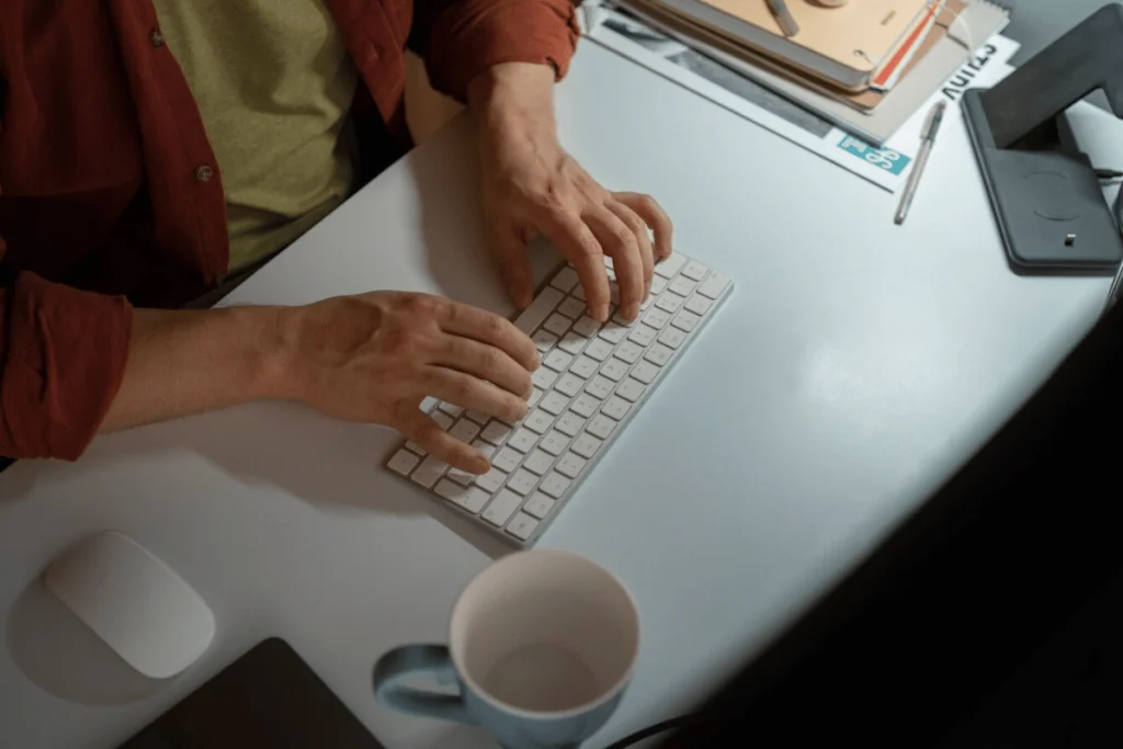 A person typing on a keyboard at a desk, with a computer screen displaying code.