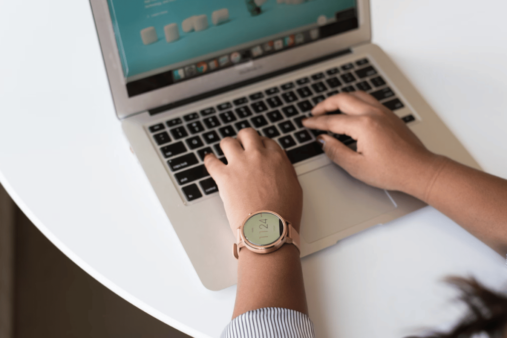 Detail of a business person's hands on a MacBook keyboard, wearing a chic wristwatch.