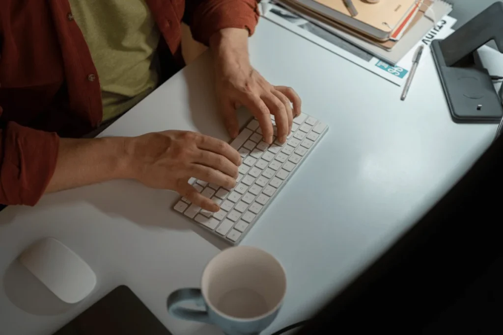 A person typing on a keyboard at a desk, focused on the screen.