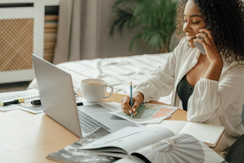 A professional is seated at a desk with a laptop, taking notes on a colorful map, surrounded by books and a cup of tea.