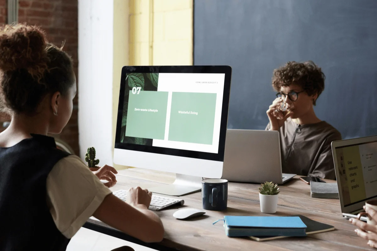 Two individuals working at computers with a presentation about sustainability on screen.