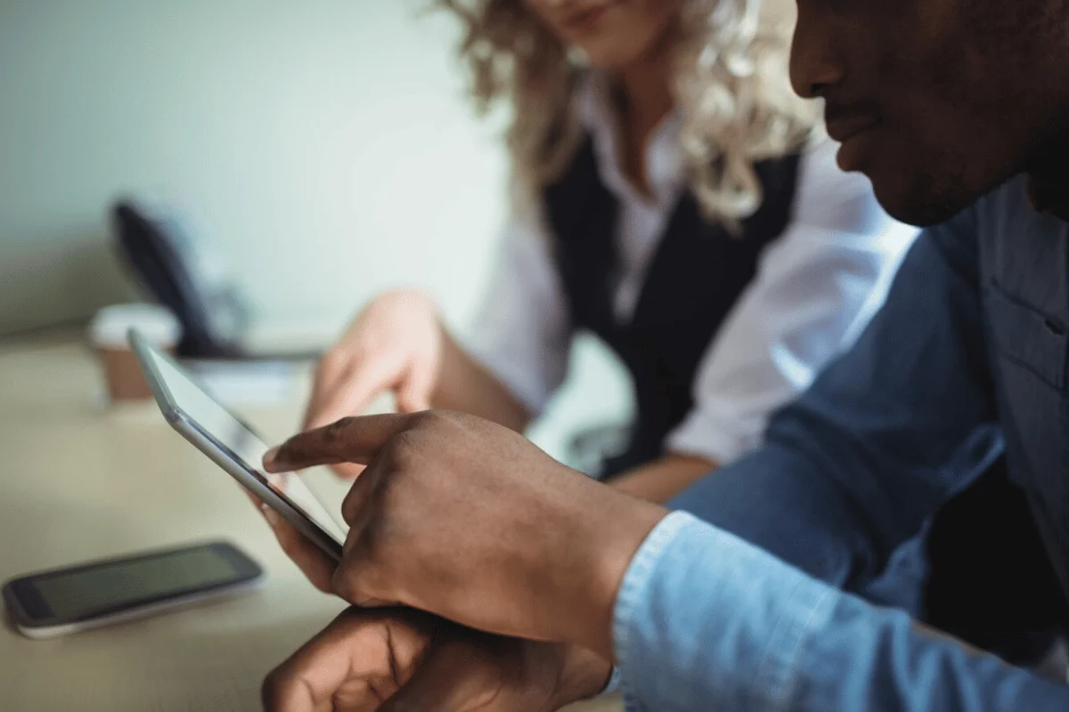 Two professionals collaborating on a tablet with a smartphone on the table.