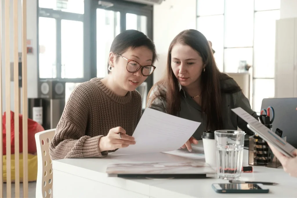 Two colleagues reviewing business documents at office desk.