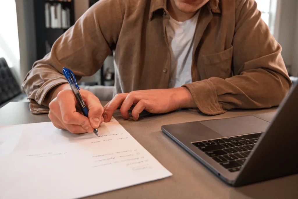 Man jotting down ideas next to a MacBook.