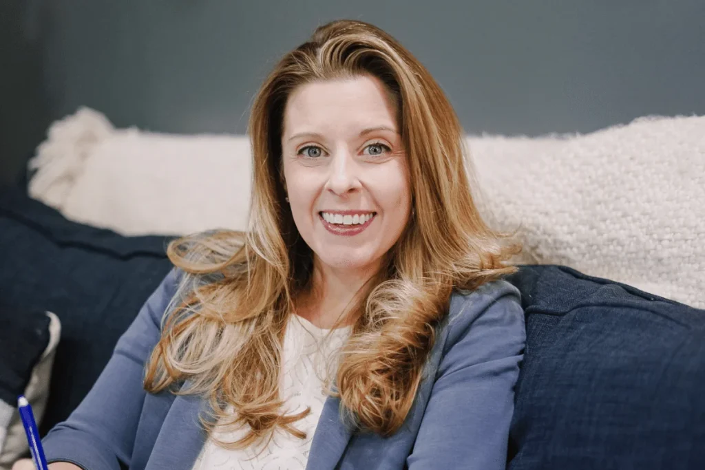 Nora Sudduth smiling warmly, seated on a navy blue couch with a striped cushion.