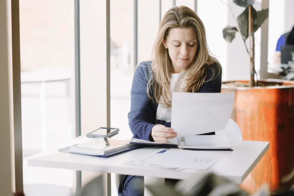 Nora examining papers beside large windows.