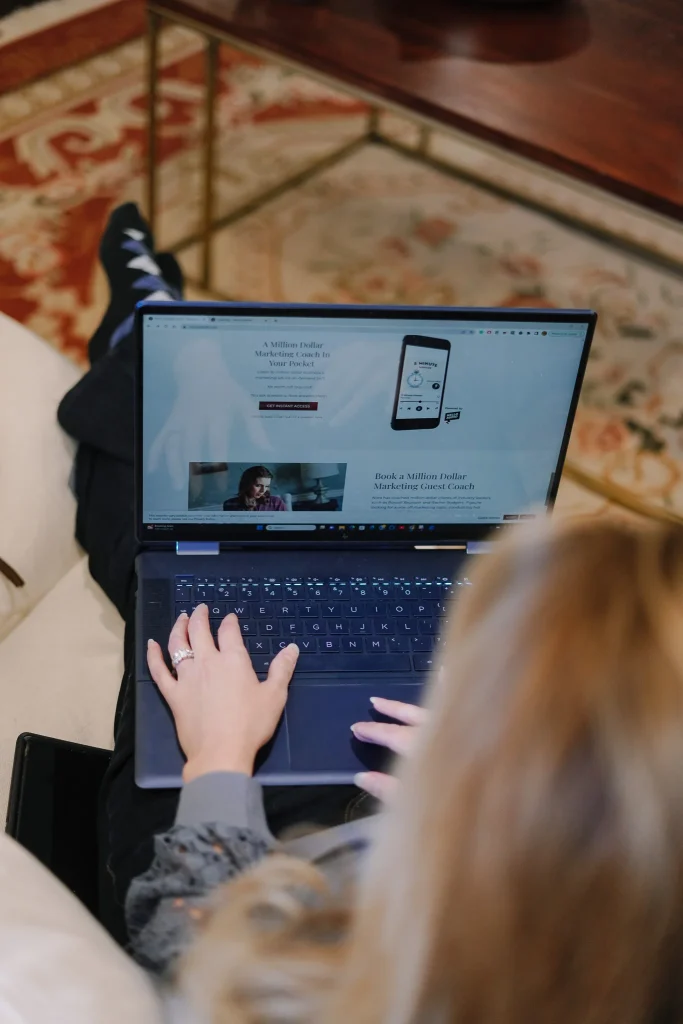 Woman browsing a marketing coaching website on her laptop while sitting on a couch.