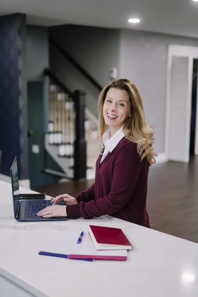 Nora working on a laptop at a modern white desk with notebooks.