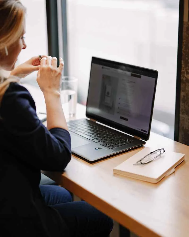 Nora sitting by the window, working on her laptop.