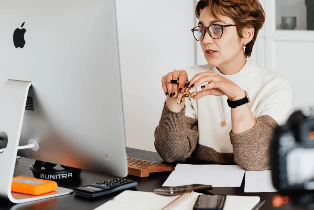 A workplace scene featuring a woman working on an Apple desktop computer.