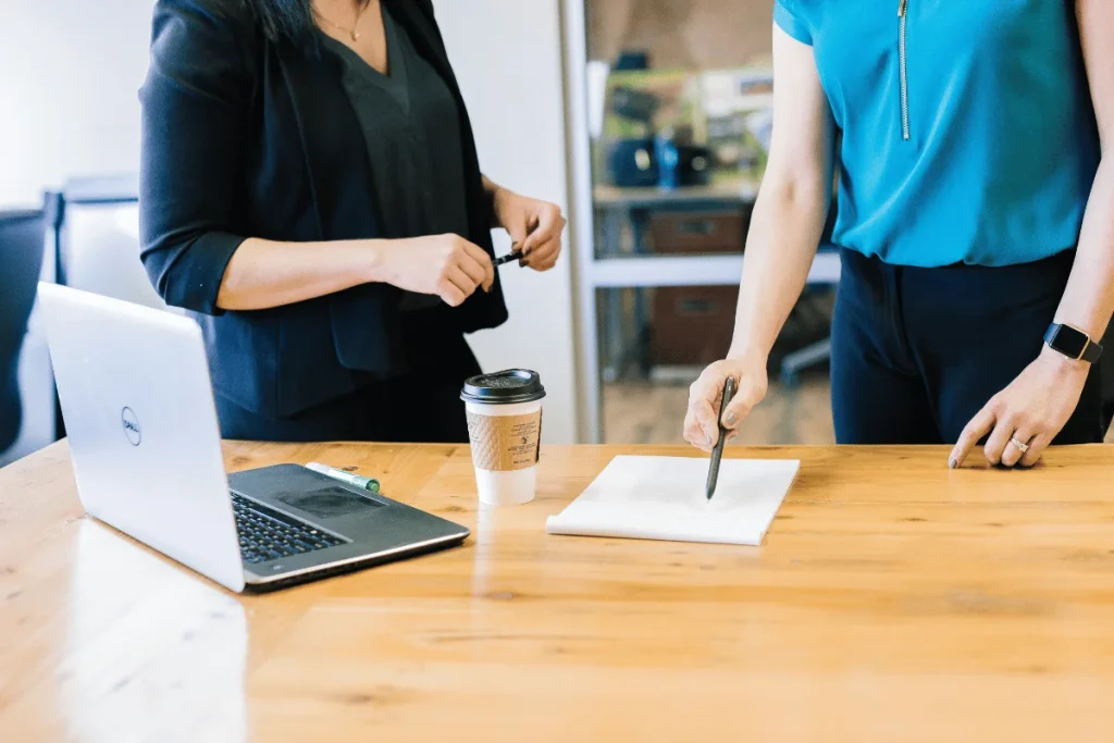Two businesswomen discussing notes at a modern office desk.