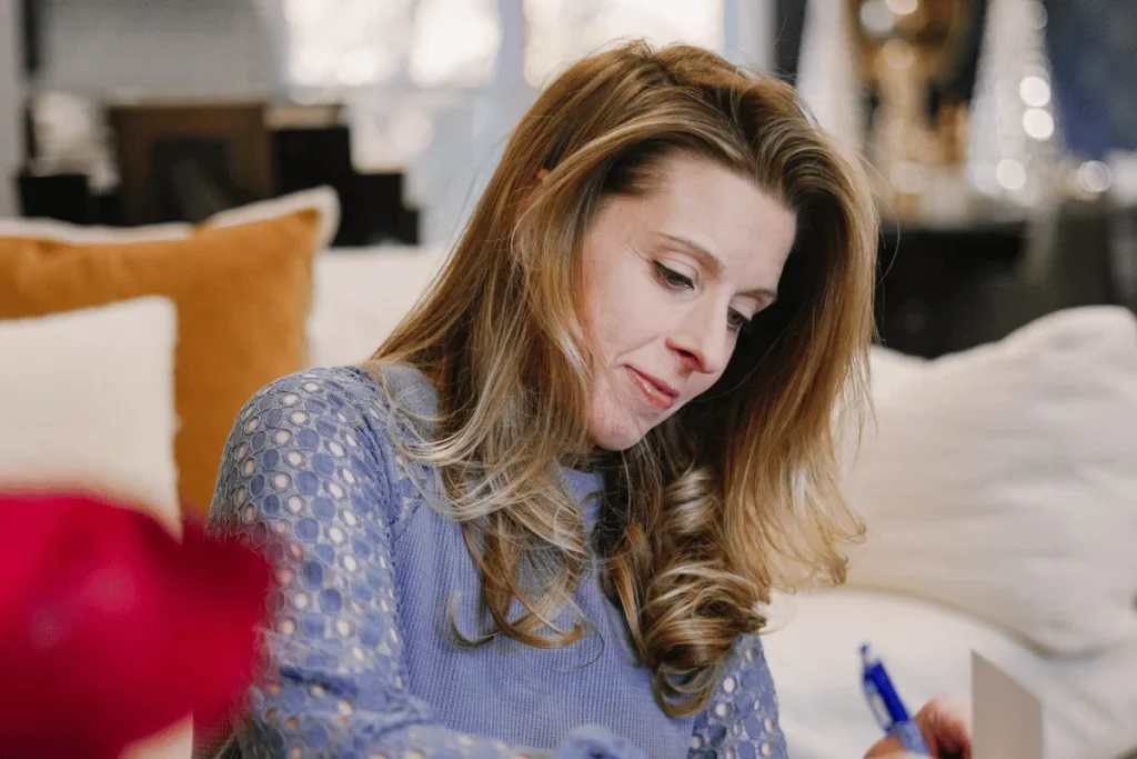 Woman in blue sweater writes on paper while seated on sofa, conveying focus and calm productivity at home.