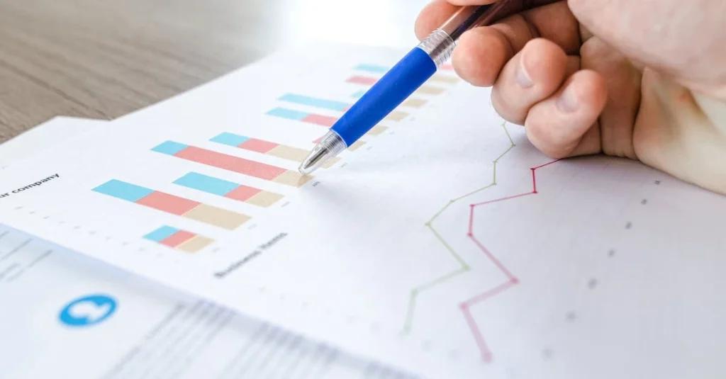 Hand pointing with blue pen at bar charts and line graphs on marketing analytics report document.