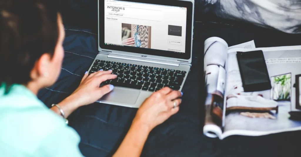 Designer working on content marketing lead generation strategy on laptop with design portfolio nearby.