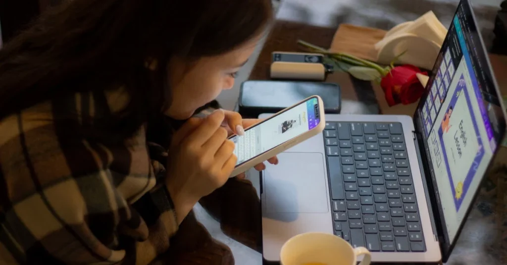 Woman reviewing smartphone data at desk with laptop and tea cup for improve marketing campaign analysis.