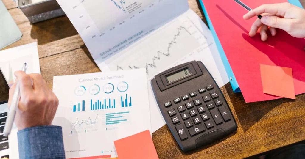 Customer acquisition consultant analyzing financial data and charts with calculator on wooden desk.