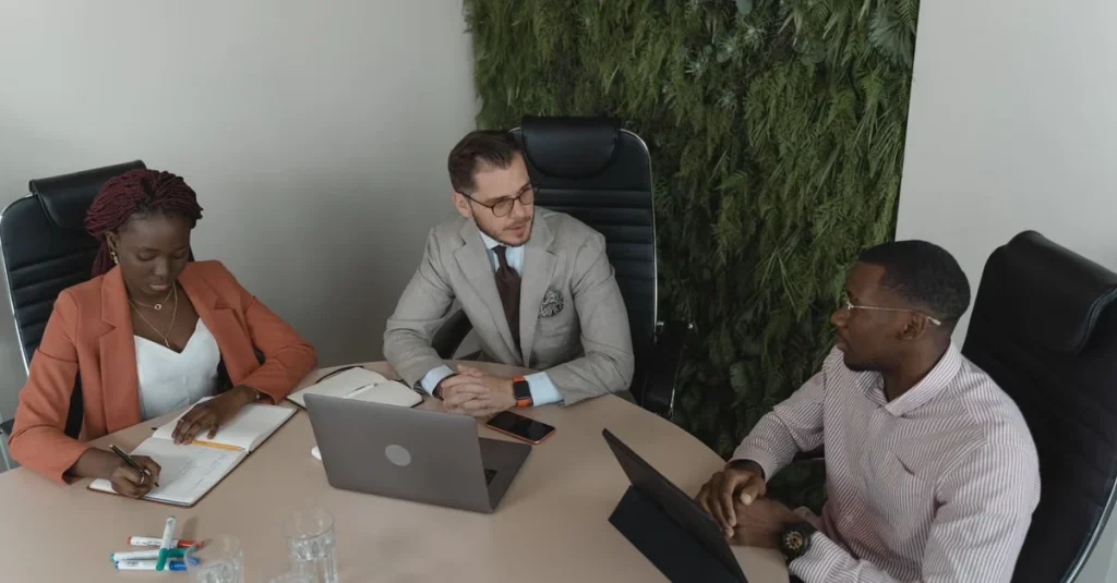 Three professionals collaborating at desk with laptop, discussing customer acquisition roadblocks and business growth.