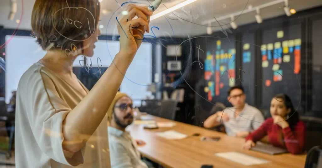 Team member writing customer acquisition roadblocks strategy on glass board during collaborative meeting session.