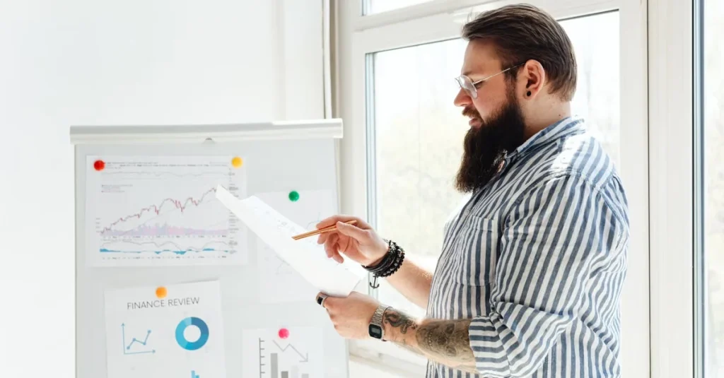 Bearded businessman analyzing customer acquisition roadblocks on whiteboard with charts and graphs.