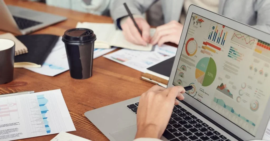 Professional analyzing customer acquisition due diligence metrics and charts on laptop at wooden desk workspace.