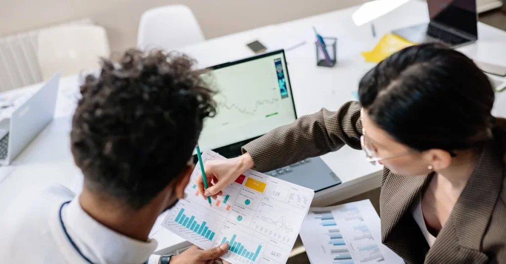 Two professionals reviewing marketing analytics charts and graphs at a conference table to improve marketing campaign.