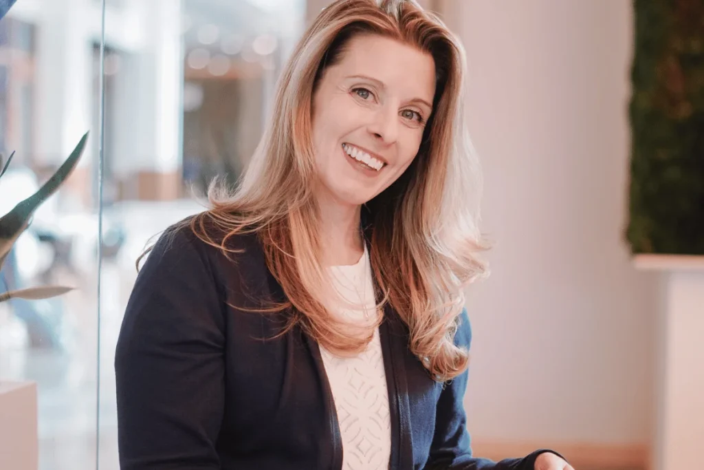 Nora Sudduth in a business casual outfit, with a joyful expression in a decorated room.