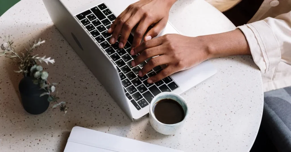 Person typing on laptop at desk with coffee and plant, creating organic content marketing strategy.
