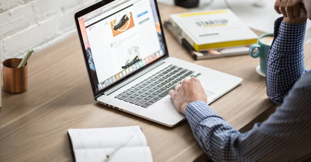 Designer working on laptop displaying organic content marketing project with notebooks and pen holder on wooden desk.